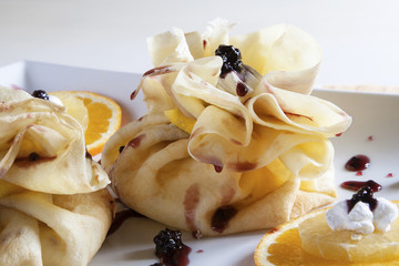 Two pancakes, wrapped as bags, with sweet filling served on a white plate with  blackberries,...