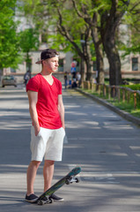 Handsome teenage boy with skateboard standing on street road