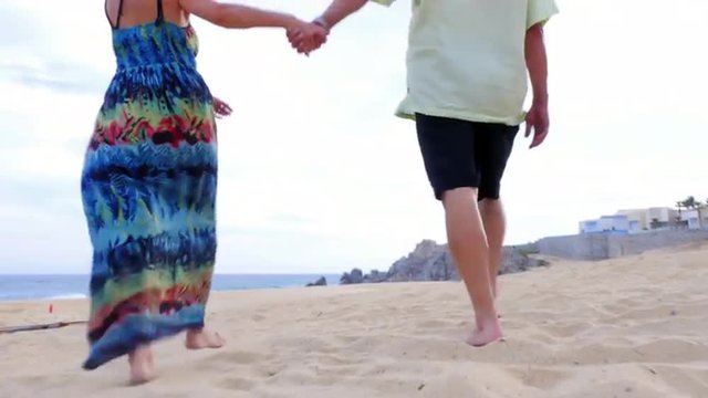 An older couple holding hands and walking on the beach 