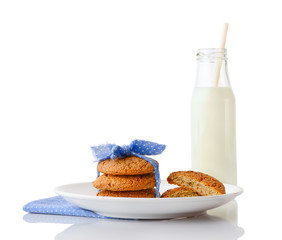 Stack of three homemade oatmeal cookies tied with blue ribbon in small white polka dots and halves of cookies on white plate on napkin and bottle of milk with straw, isolated on white background