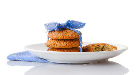 Stack of three homemade oatmeal cookies tied with blue ribbon in small white polka dots and bitten cookie on white ceramic plate on matching blue napkin, isolated on white background