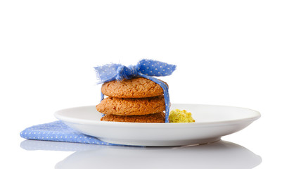 Stack of three homemade oatmeal cookies tied with blue ribbon in small white polka dots and tiny yellow flowers on white ceramic plate on matching blue napkin, isolated on white background
