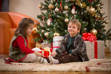 Cute little children opening Christmas presents in front of the Christmas tree