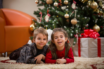Fototapeta na wymiar Cute happy children lying on the floor in front of the Christmas tree
