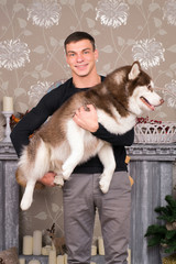 A nice young man is keeping on his hand a Husky dog at New Year