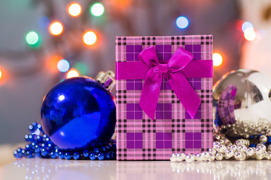 Purple checkered gift box with bow and Christmas balls with garland lights on background. Festive New Year decoration