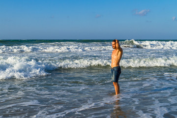 Young attractive man enjoys spalshing in ocean water at dusk.
