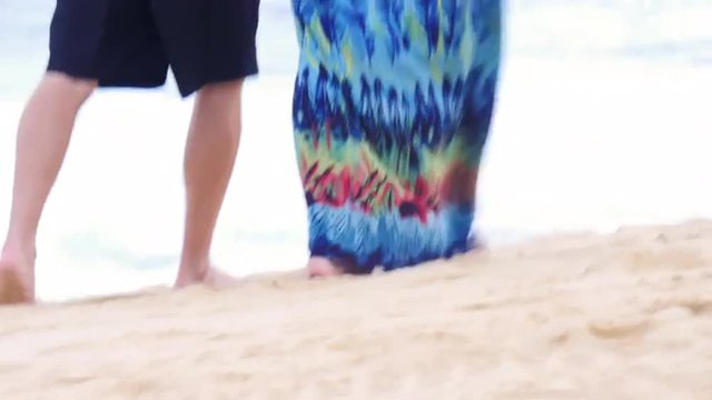 An older couple holding hands and walking down the beach, starting close up on their feet