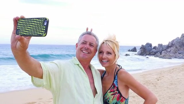 An older couple having fun and taking selfies on the beach
