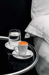 Espresso coffee full cup and glass of water on bedside table closeup