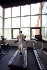 Muscular man running on a treadmill in a fitness club, sport in