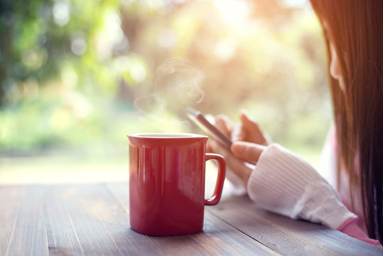 Hot of coffee red cup on wood table. rear view of female hand holding smart phone. Photo in vintage color image style.