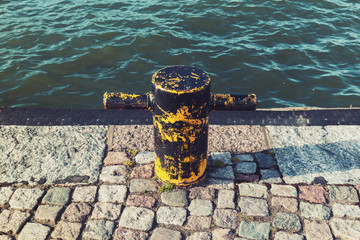 Naklejka premium Old rusted yellow mooring bollard on stone pier