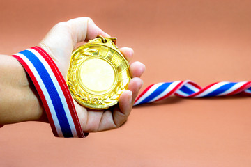old gold medal in hand the winner on brown background, blank fac