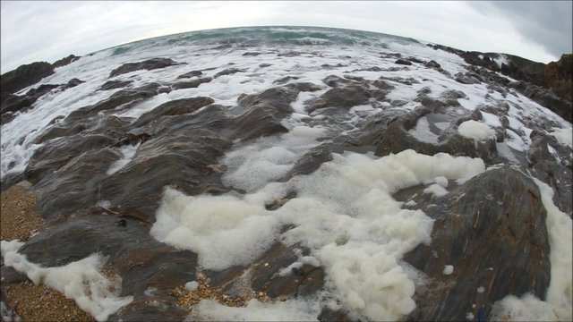 Brandung rauscht &uuml;ber runde Felsen mit Schaum &ndash; gefilmt durch Fisheye