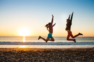Fototapeta na wymiar Couple jumps on the beach over sunrise