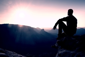 Hiker take relaxing on a rock and enjoying sunset at horizon. Vivid effect.