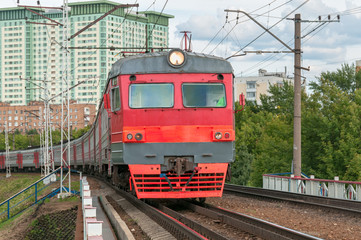 Plakat Red and grey suburban electric train moves towards on railroad turn vanishing against skyline background. Moscow, Russia. 