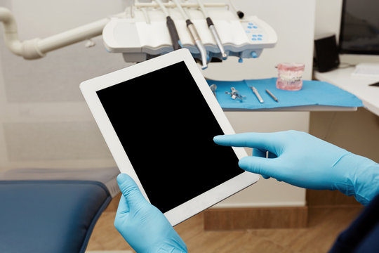 Dentist working on tablet pc at the dental clinic. White tablet with a blank screen