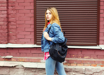 young girl wearing a jeans jacket and black bag walking in city