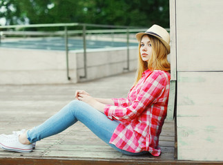 young girl wearing a pink shirt and summer hat sitting in city