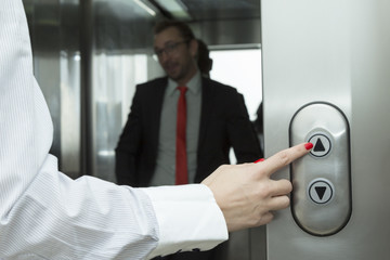 Naklejka na ściany i meble Female hand pressing elevator up button. Businessman inside of the elevator.