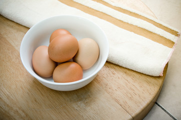 the five eggs in white ceramic bowl and brown strip white towel on wood table
