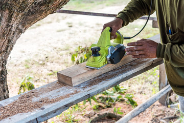 worker planing a plank of wood with a electric plane