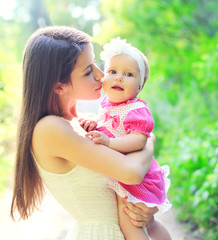 Happy mother hugging and kissing baby in summer day