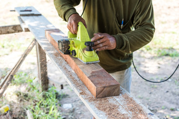 worker planing a plank of wood with a electric plane
