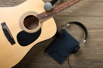 Acoustic guitar, headphones, notebook and microphone on wooden background, close up
