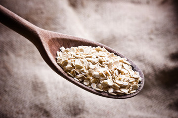 Oat flakes on wooden spoon on linen fabric texture.