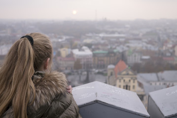 Thoughtful young girl against a city by dusk. Sight of a city at the dusk.