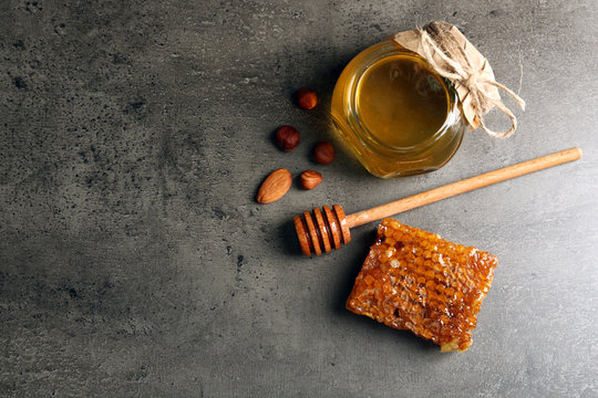 Honeycomb, glass pot with honey and nuts on gray background