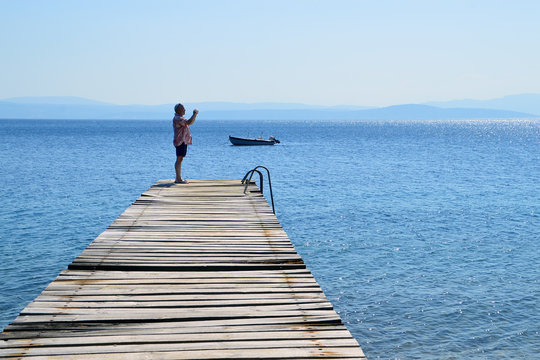 Man on an old wooden pier taking photo with his phone