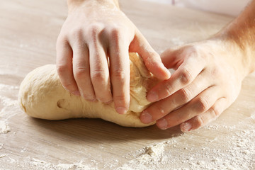 Hands kneading dough for pizza on the wooden table, close-up