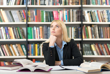 young woman sitting in the library with books around dreaming