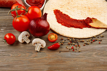 Dough basis and ingredients for pizza in the shape of circle, on the table