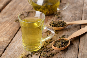 Glass cup of tea and teapot on wooden background