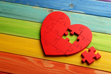 Red puzzle heart on colorful wooden background