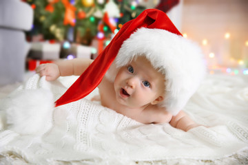 Naked baby in red hat on the floor in the decorated Christmas room