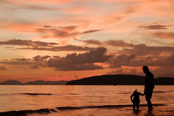 Silhouette image of father and his child by the sea shore, sunset
