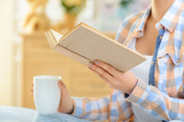 Girl is drinking tea and reading book.
