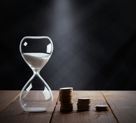 Hourglass with coins on wooden table on black background