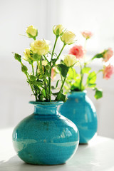 Beautiful roses in turquoise vases on window background