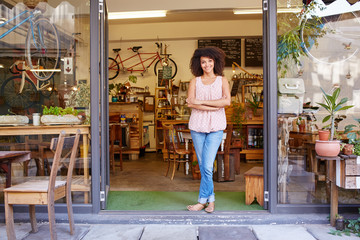 Woman standing happily in the entrance of her coffee shop