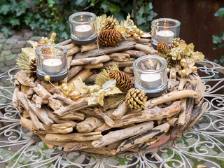 Christmas centerpiece with candles and cones on outdoor irony table, brown and gold colors.