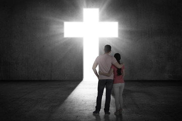 Young couple looking the shining cross on the wall