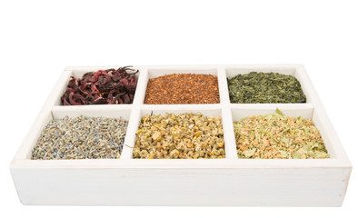Dried herbal tea leaves, lavender, rooibos, chamomile, linden flower, hibiscus, Japanese green tea in white wooden box over white background