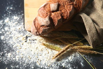 rustic crusty bread and wheat ears on a dark wooden table